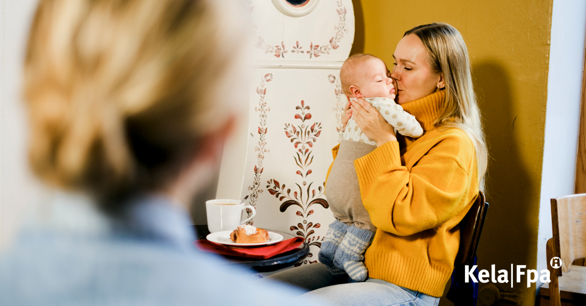 Äiti pitää vauvaa sylissään. He istuvat kahvilassa.