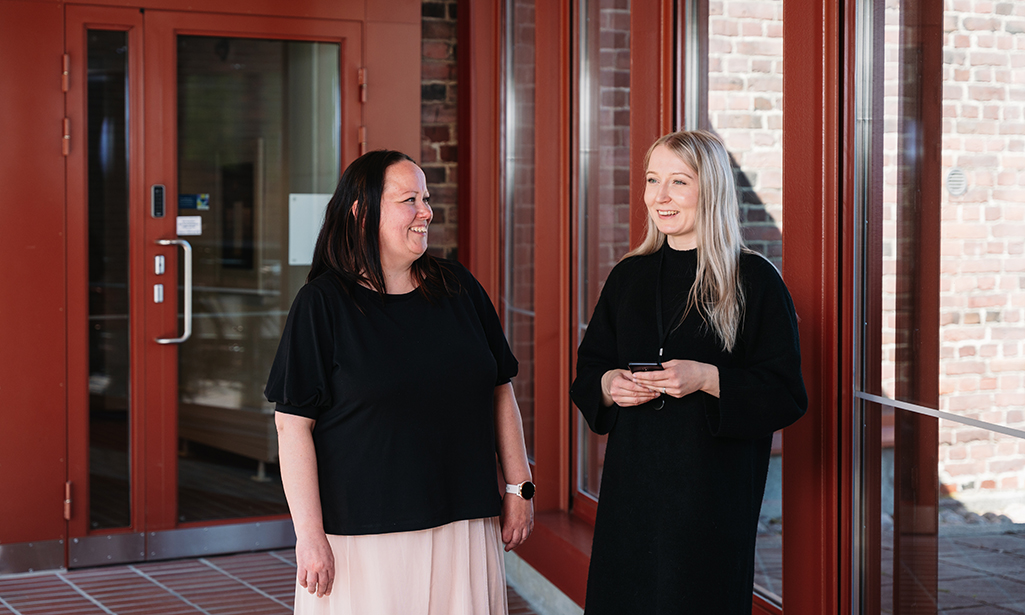 Sanna-Riikka Salonen ja Riia Aarnio seisovat Valtion talous- ja henkilöstöhallinnon palvelukeskuksen oven edessä.